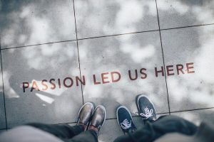 two-people-standing-over-a-sign-that-says-passion-led-us-here