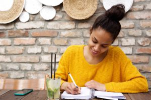 Beautiful young black woman writing notes at cafe