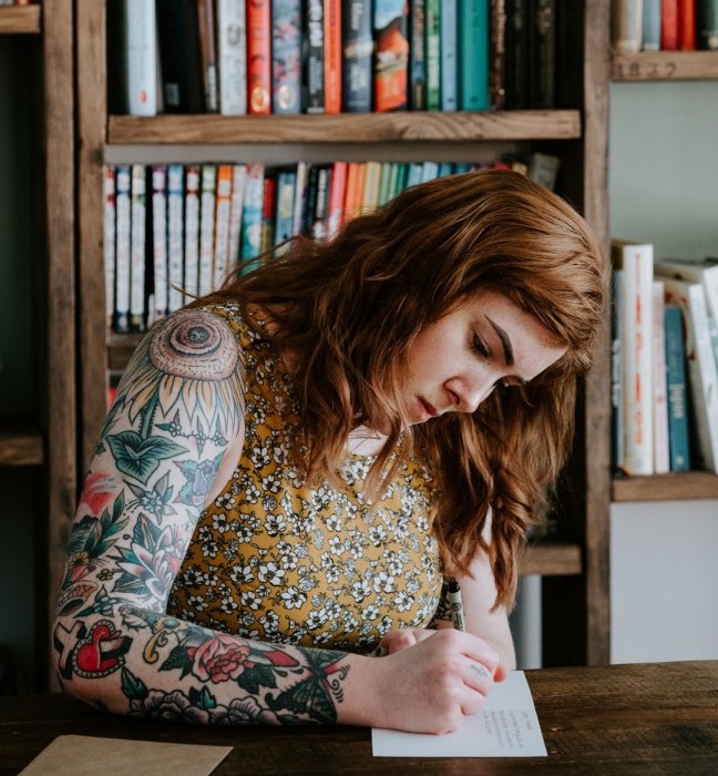 caucasian woman with tattoos writing in journal