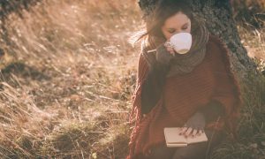 woman writing and drinking coffee beneath tree