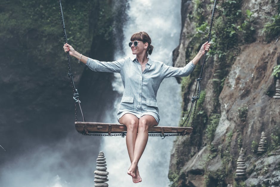 smiling woman on swing over waterfall and cliffs